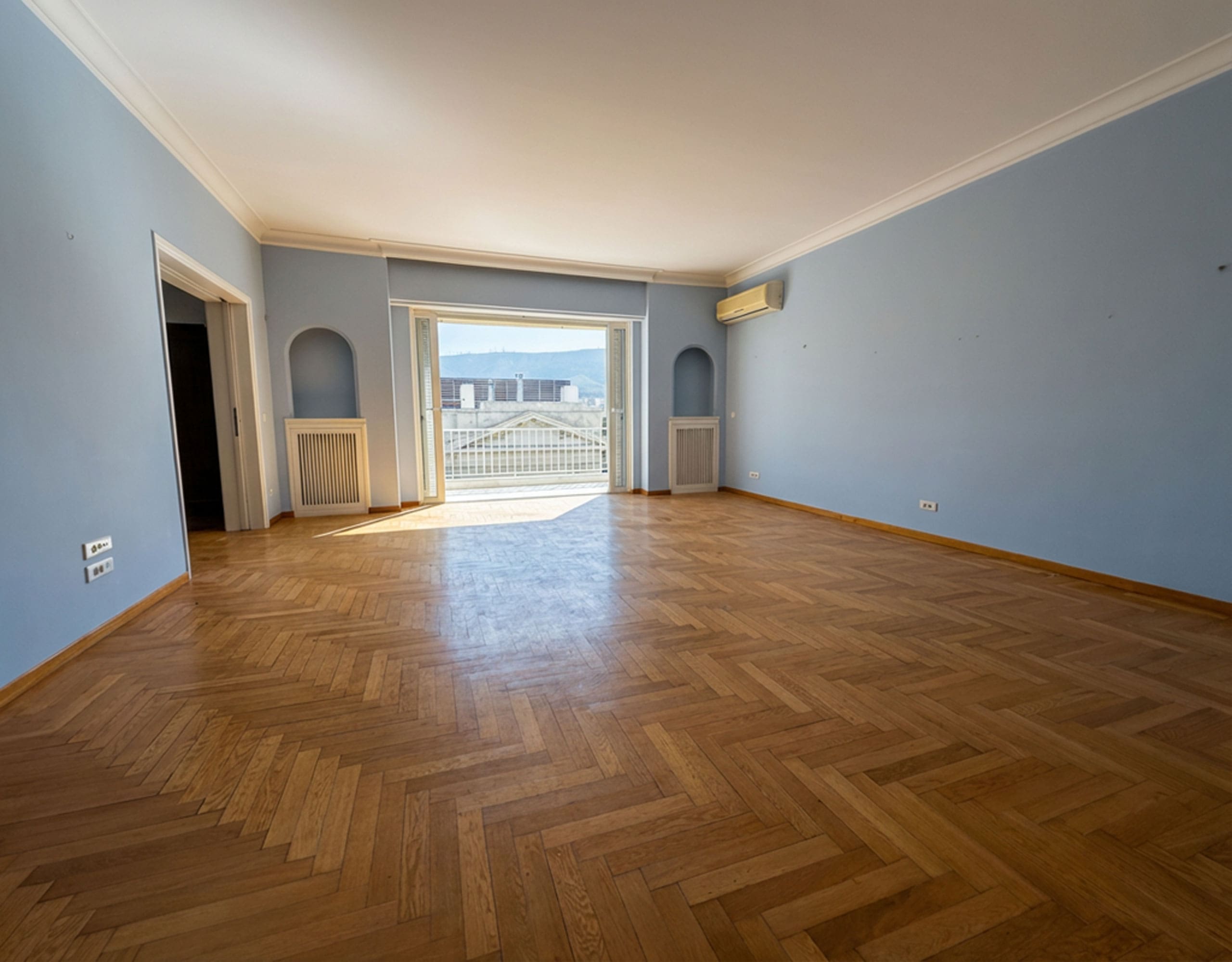 Spacious empty living room with herringbone wood flooring and balcony doors, Anaktora, Kolonaki, Athens, Greece