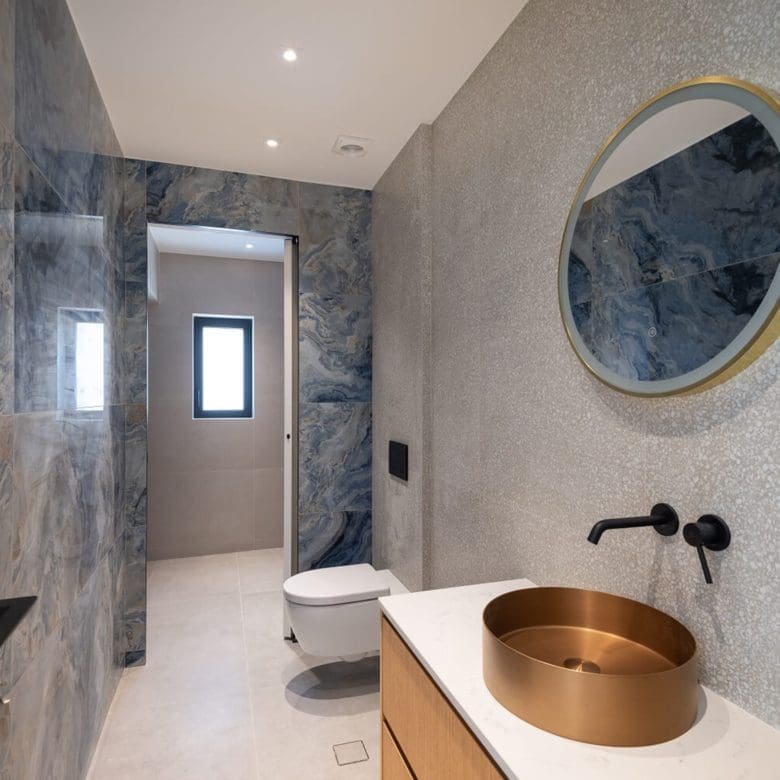 Modern bathroom with round mirror, stone-textured walls, and wall-mounted basin, Athens Riviera, Greece