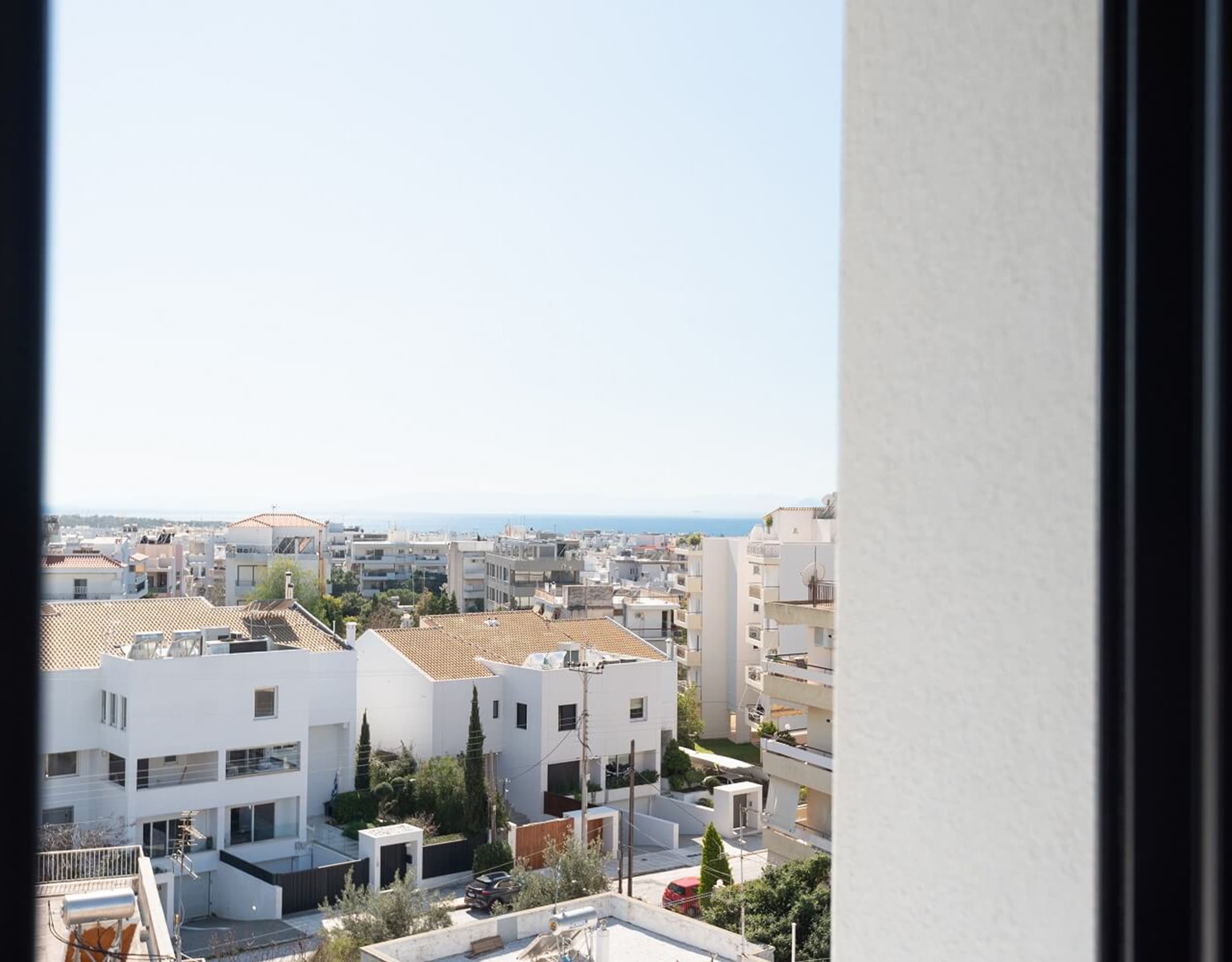 View through a window toward rooftops and distant sea horizon, Athens Riviera, Greece