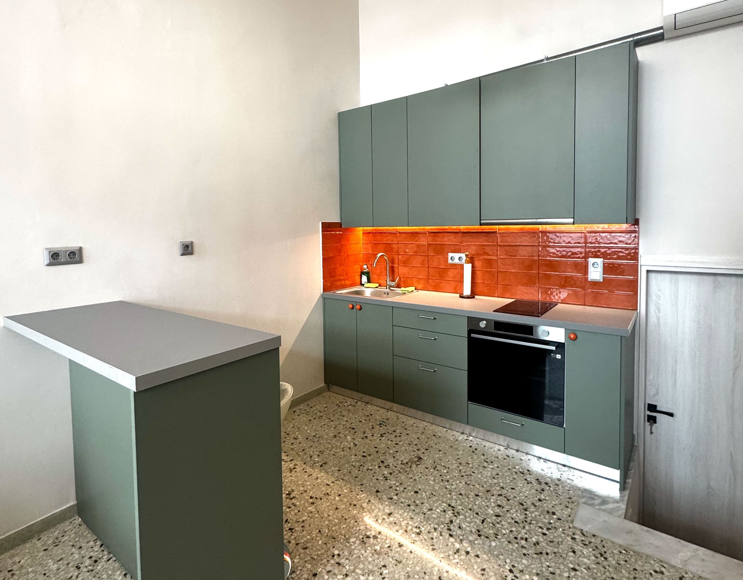 Pangrati Investment Apartment 51 sqm – Kitchen With Green Cabinetry Modern kitchen with green cabinetry, peninsula counter, and orange tile backsplash, Pangrati, Athens, Greece