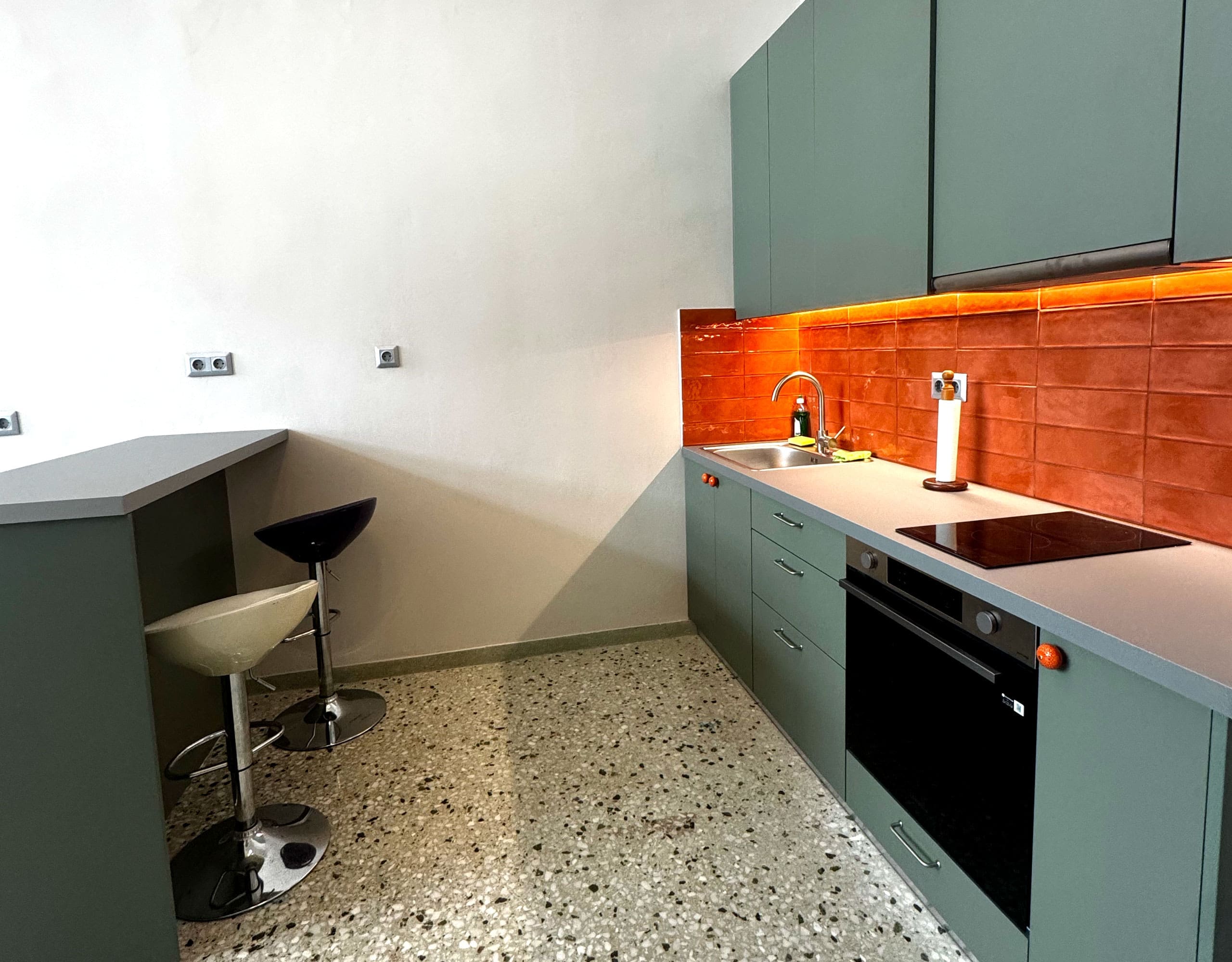 Pangrati Investment Apartment 51 sqm – Kitchen Detail With Bar Stool Kitchen detail with green cabinets, bar stool, and orange tile backsplash, Pangrati, Athens, Greece
