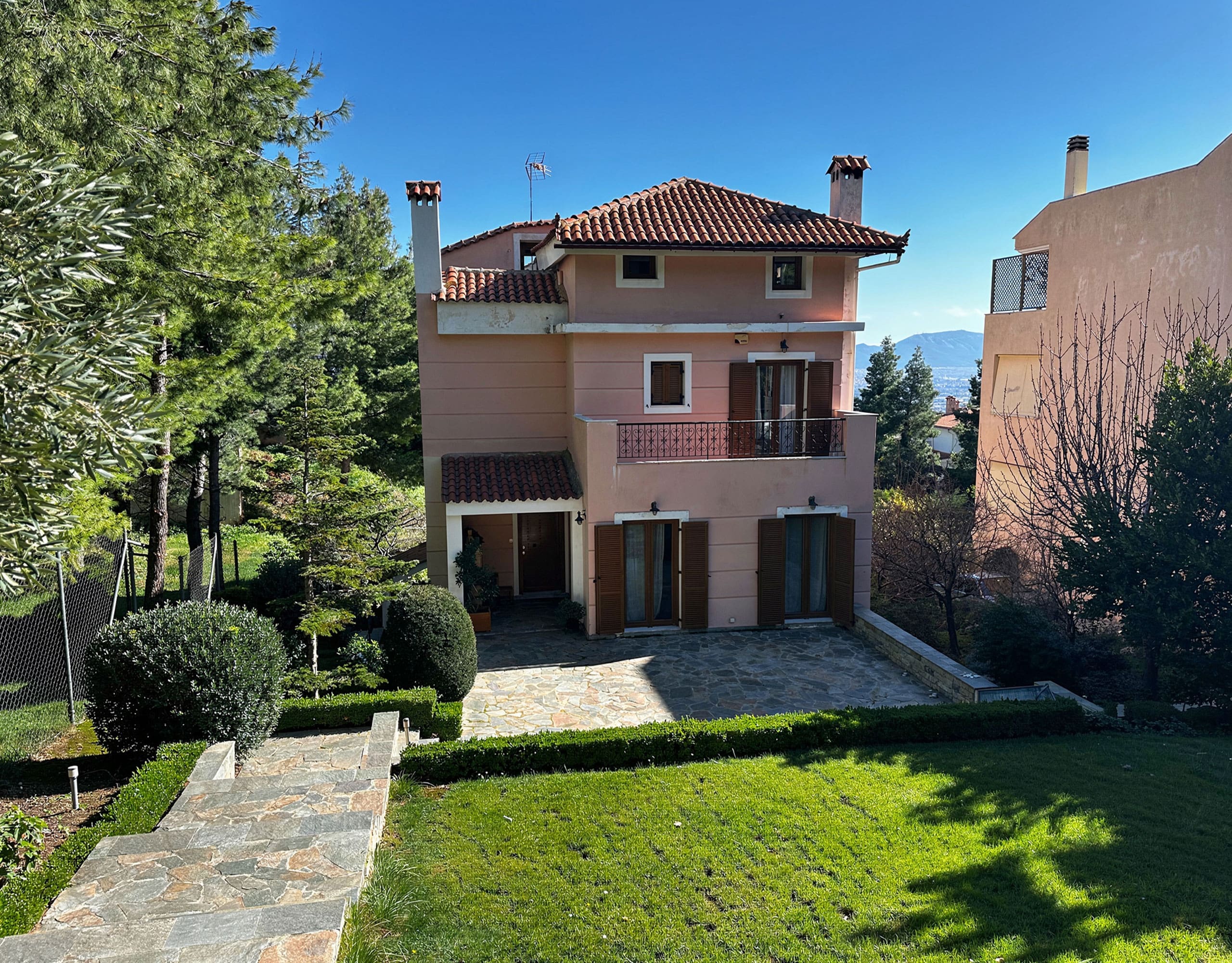 Exterior view of the detached residence with garden lawn and paved path, Thrakomakedones, Athens, Greece