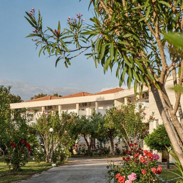 Hotel exterior with garden path, trees, and flowering plants, Skala Kallonis, Lesvos, Greece