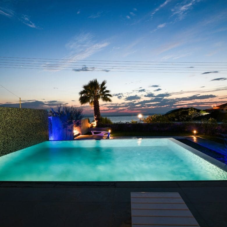 Infinity pool at dusk with palm silhouettes and open horizon view, Sounio, Athens Riviera, Greece