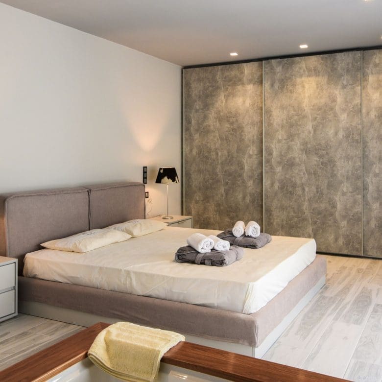 Bedroom with double bed, neutral decor, and textured accent wall, Sounio, Athens Riviera, Greece