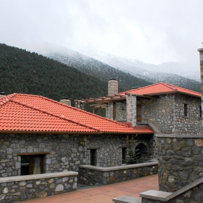 View across stone buildings with red-tiled roofs and forested mountain slopes, Kardaras, Mount Mainalo, Arcadia, Greece