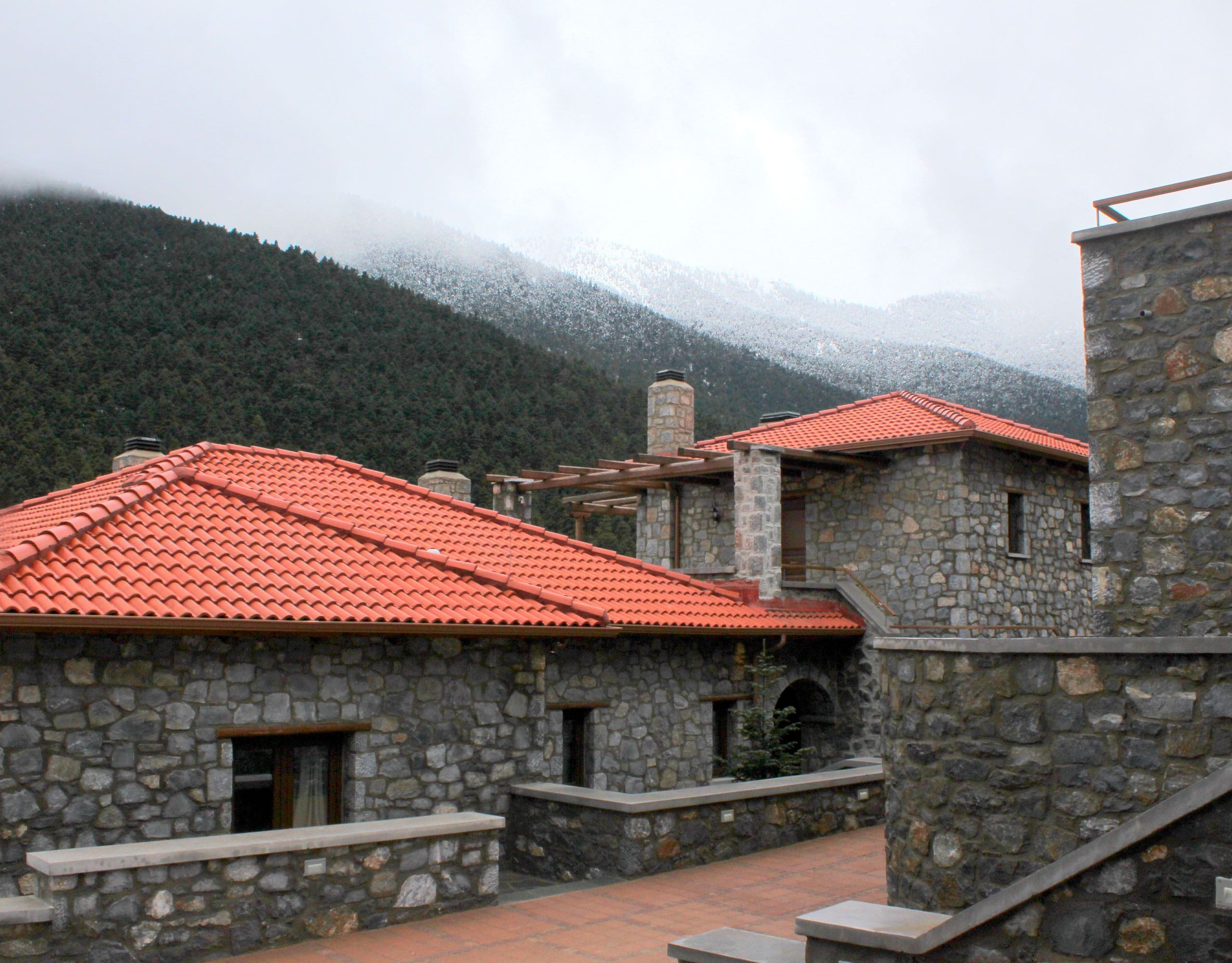 View across stone buildings with red-tiled roofs and forested mountain slopes, Kardaras, Mount Mainalo, Arcadia, Greece