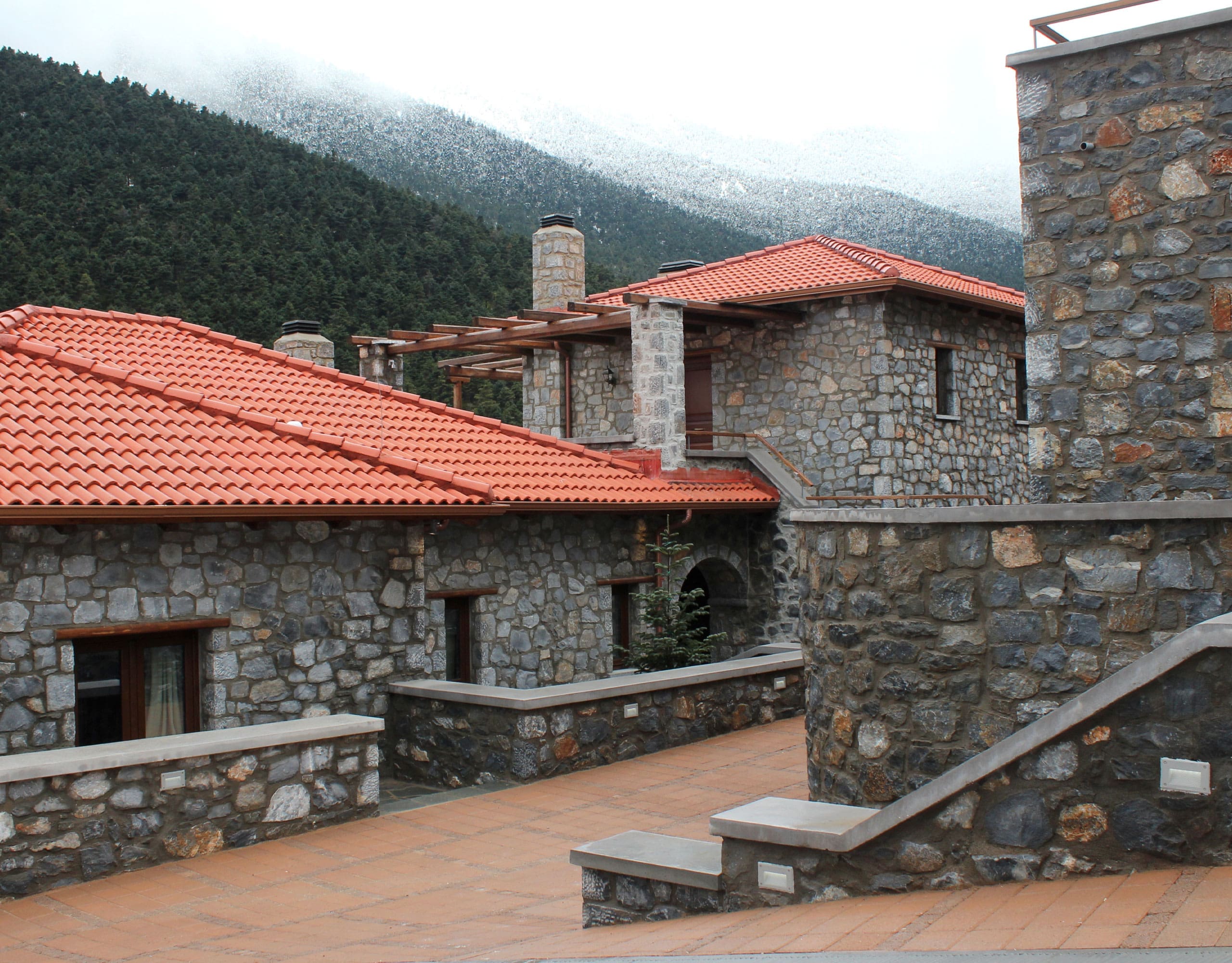 View across stone buildings with red-tiled roofs and forested mountain slopes, Kardaras, Mount Mainalo, Arcadia, Greece