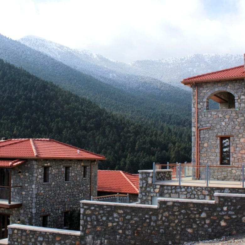 Stone-built hotel exterior with red roofs and misty mountain background, Kardaras, Mount Mainalo, Arcadia, Greece