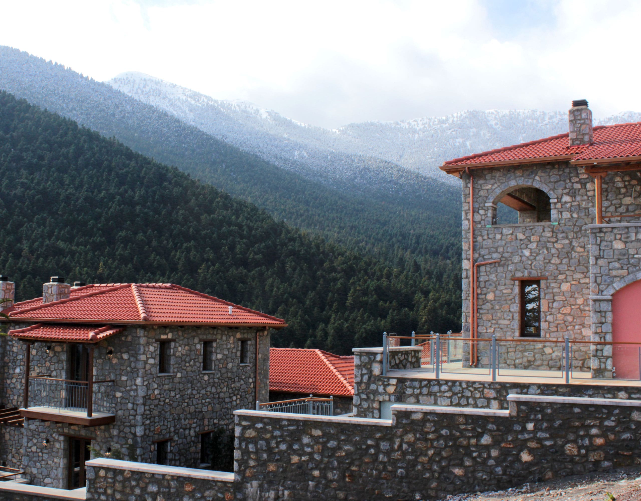 Stone-built hotel exterior with red roofs and misty mountain background, Kardaras, Mount Mainalo, Arcadia, Greece