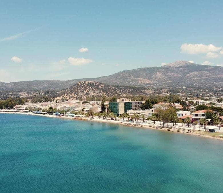 Aerial coastal view with turquoise sea, shoreline promenade, and mountains in the background