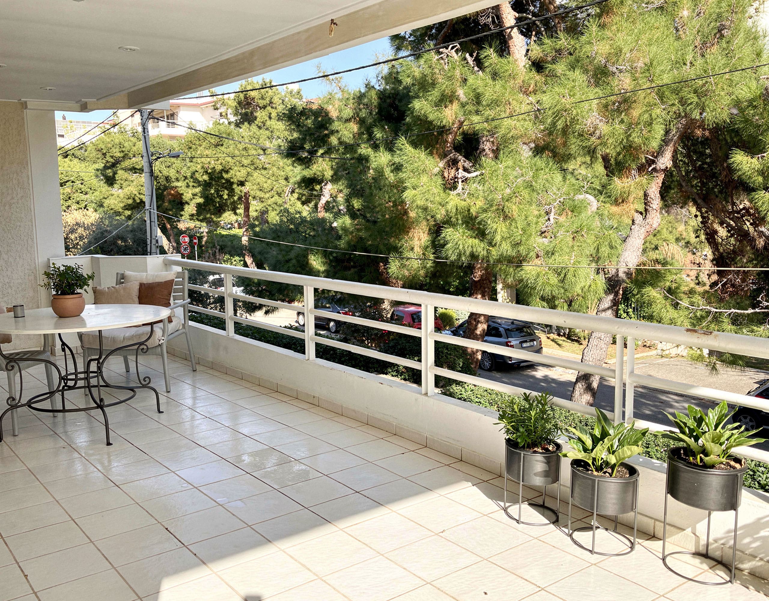 Voula Duplex 181 sqm – Covered Balcony Dining Area Covered balcony with outdoor dining table, railing, and greenery views, Voula, Athens Riviera, Greece