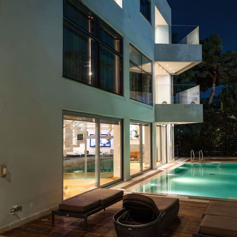 Private pool area at night with illuminated villa façade in Alimos, Athens Riviera