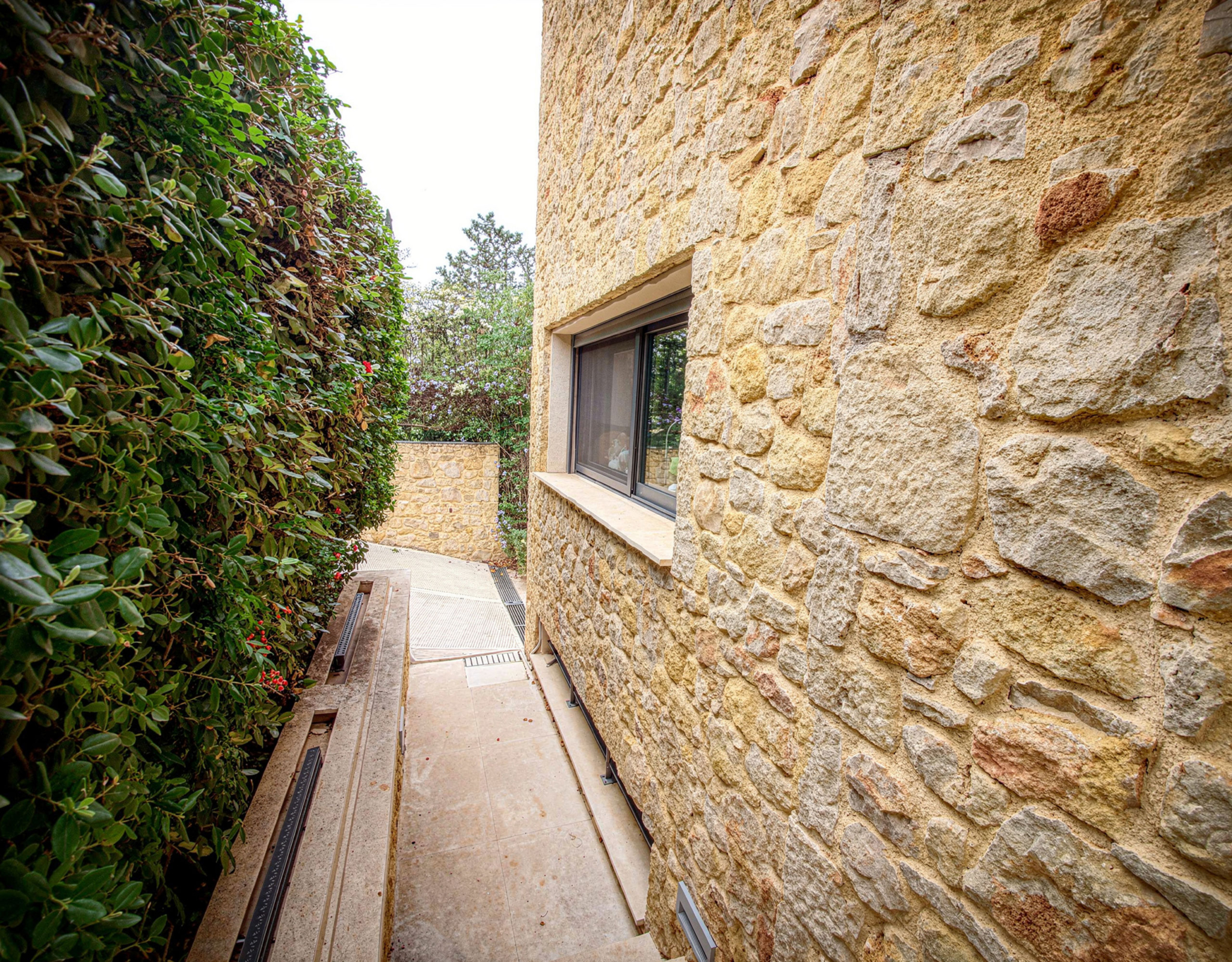 Narrow outdoor side passage with stone wall and greenery, Porto Rafti, Greece
