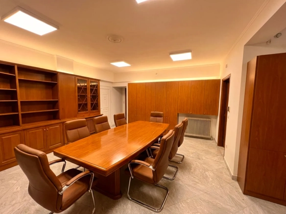 Wood-paneled conference room with a long table, brown leather chairs, and wall-to-wall cabinets.