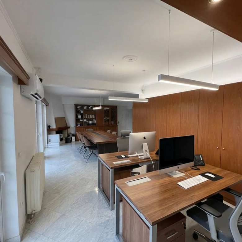 Bright, open office with a long wooden conference table, ergonomic chairs, and tall wooden storage cabinets along the wall.