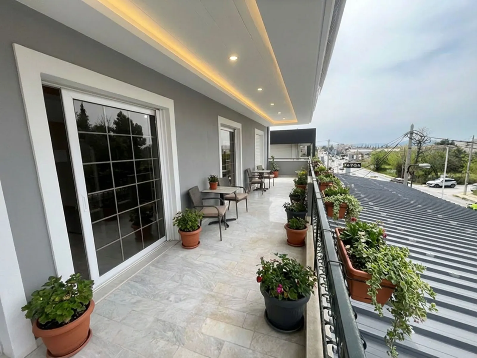 Balcony with potted plants, seating, and sliding glass doors along a gray building.
