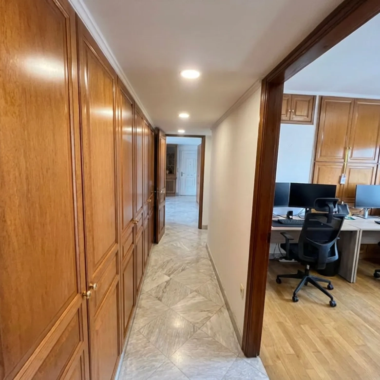 Long hallway with tall wooden cabinets lining the left wall and an open office area with desks and computers on the right.