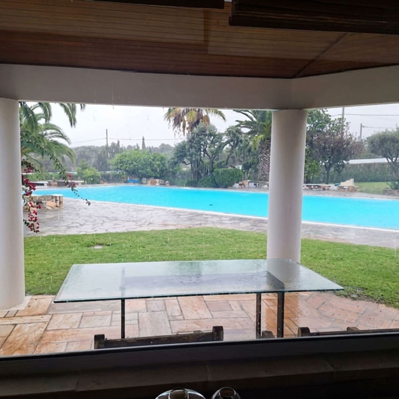 Covered terrace looking out to the swimming pool and garden at a private estate in Porto Rafti, Attica