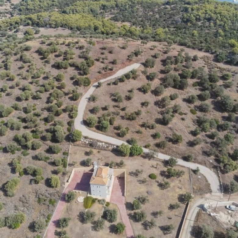 Drone view of the land plot with winding access road and olive grove terrain, Ermioni, Greece