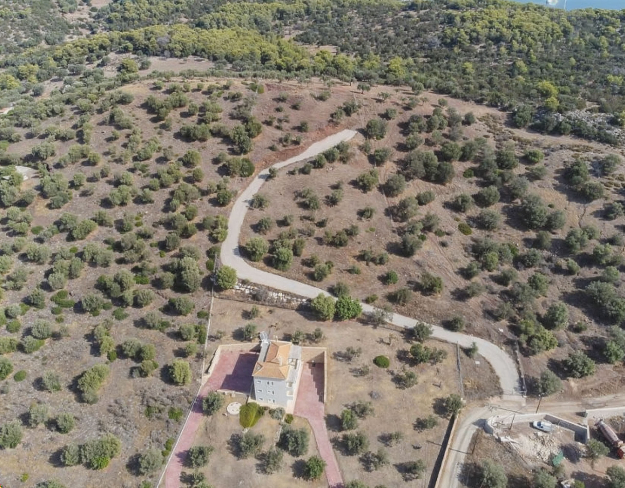 Ermioni Seaview Land Plot – Winding Road And Olive Grove View Drone view of the land plot with winding access road and olive grove terrain, Ermioni, Greece