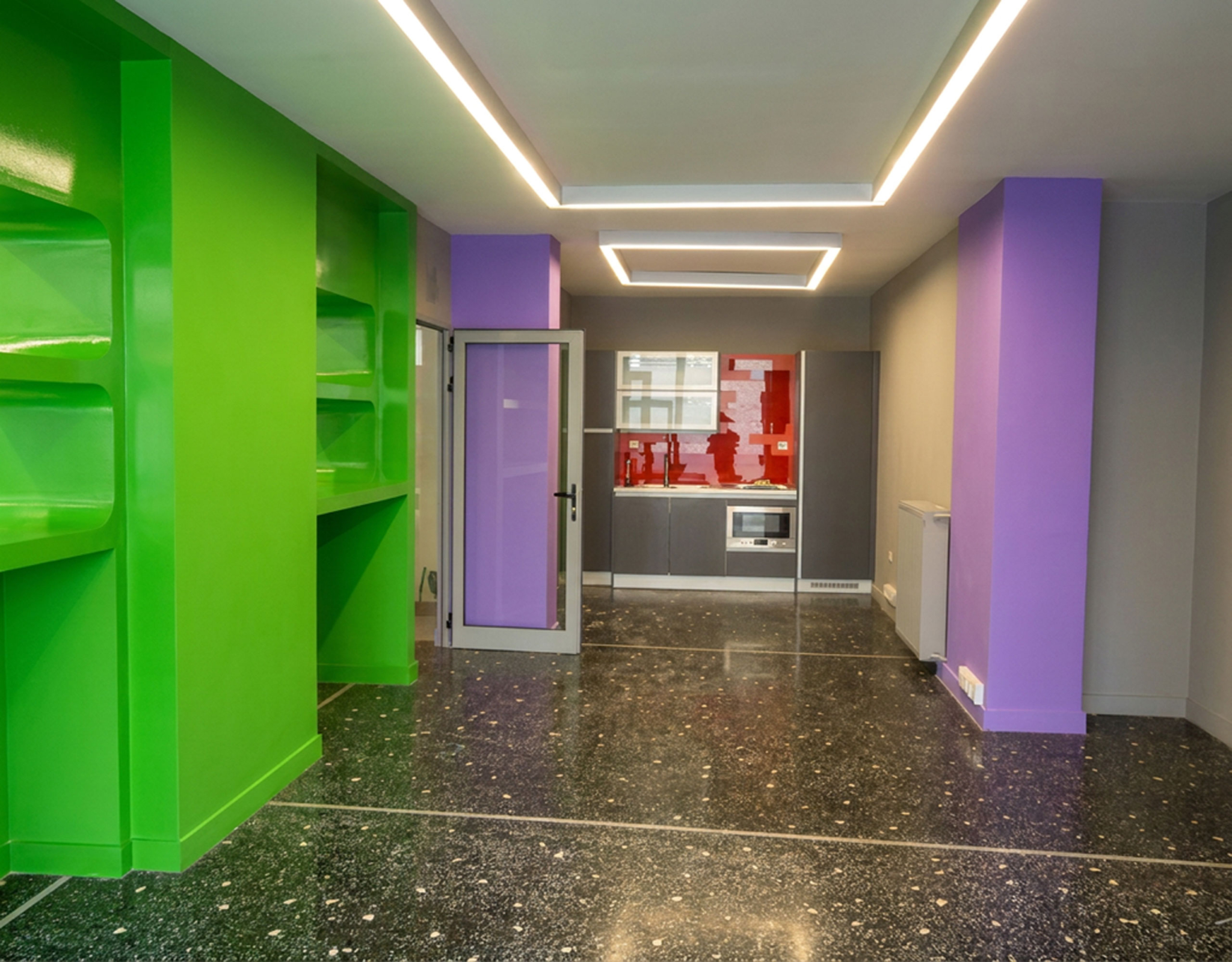 Open-plan εσωτερικός χώρος με ειδικό φωτισμό οροφής, ενσωματωμένα ράφια και κουζίνα στο βάθος σε εμπορικό ακίνητο στο κέντρο Θεσσαλονίκης